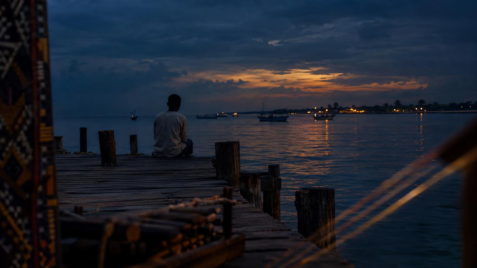 Dusk on a Gulf of Guinea jetty with a lone figure, textile patterns at the edges and abstract balafon and string motifs.